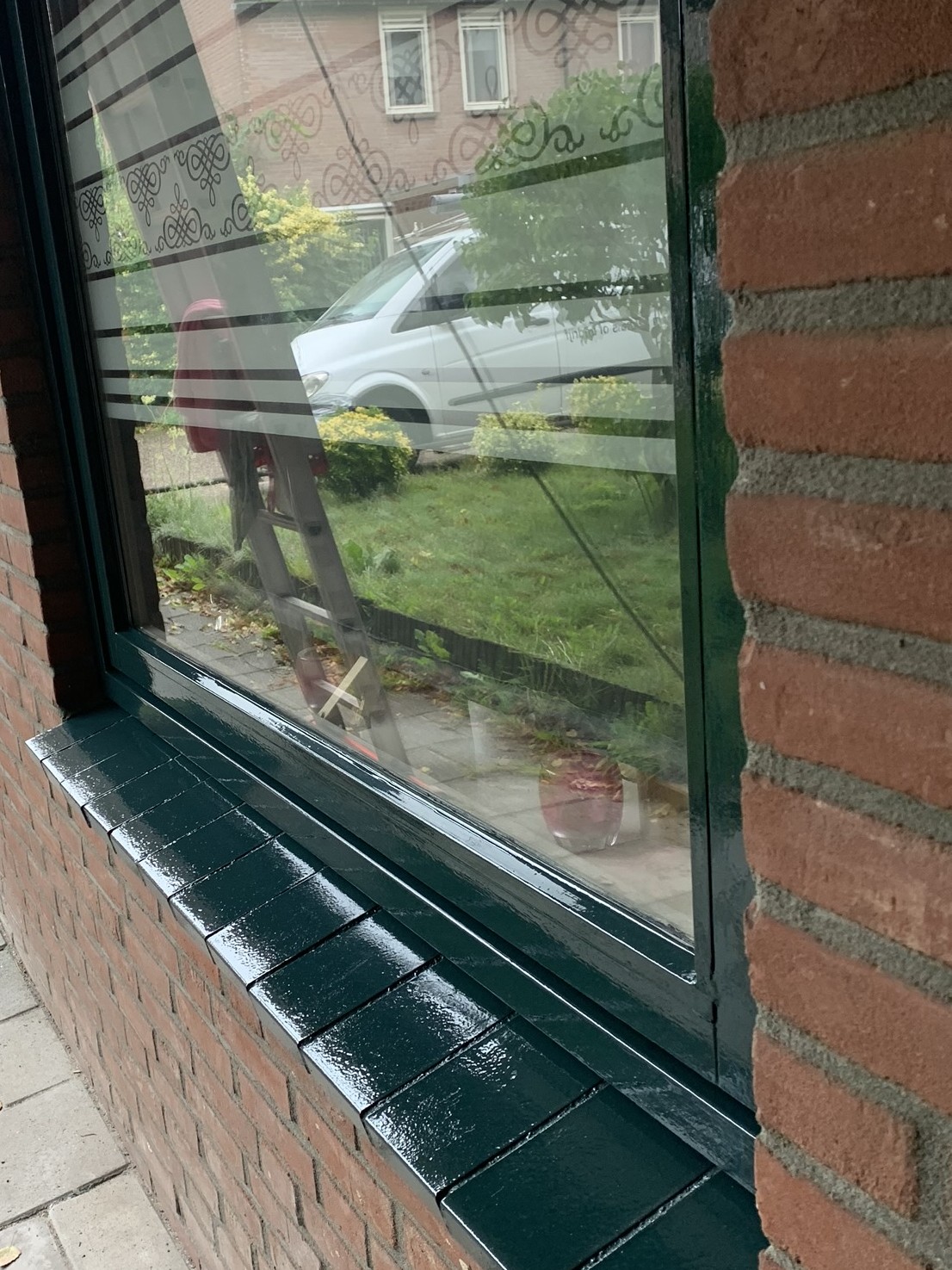 Kozijn en vensterbank in glanzende donkergroene lak, in een rode bakstenen gevel