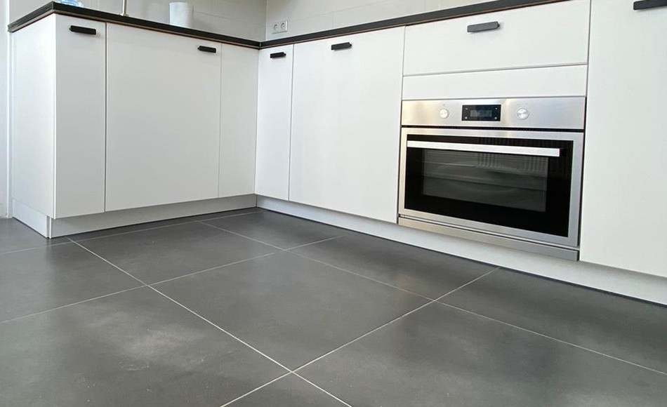 Witte keuken met zwart werkblad, inbouwoven en grote grijze vloertegels