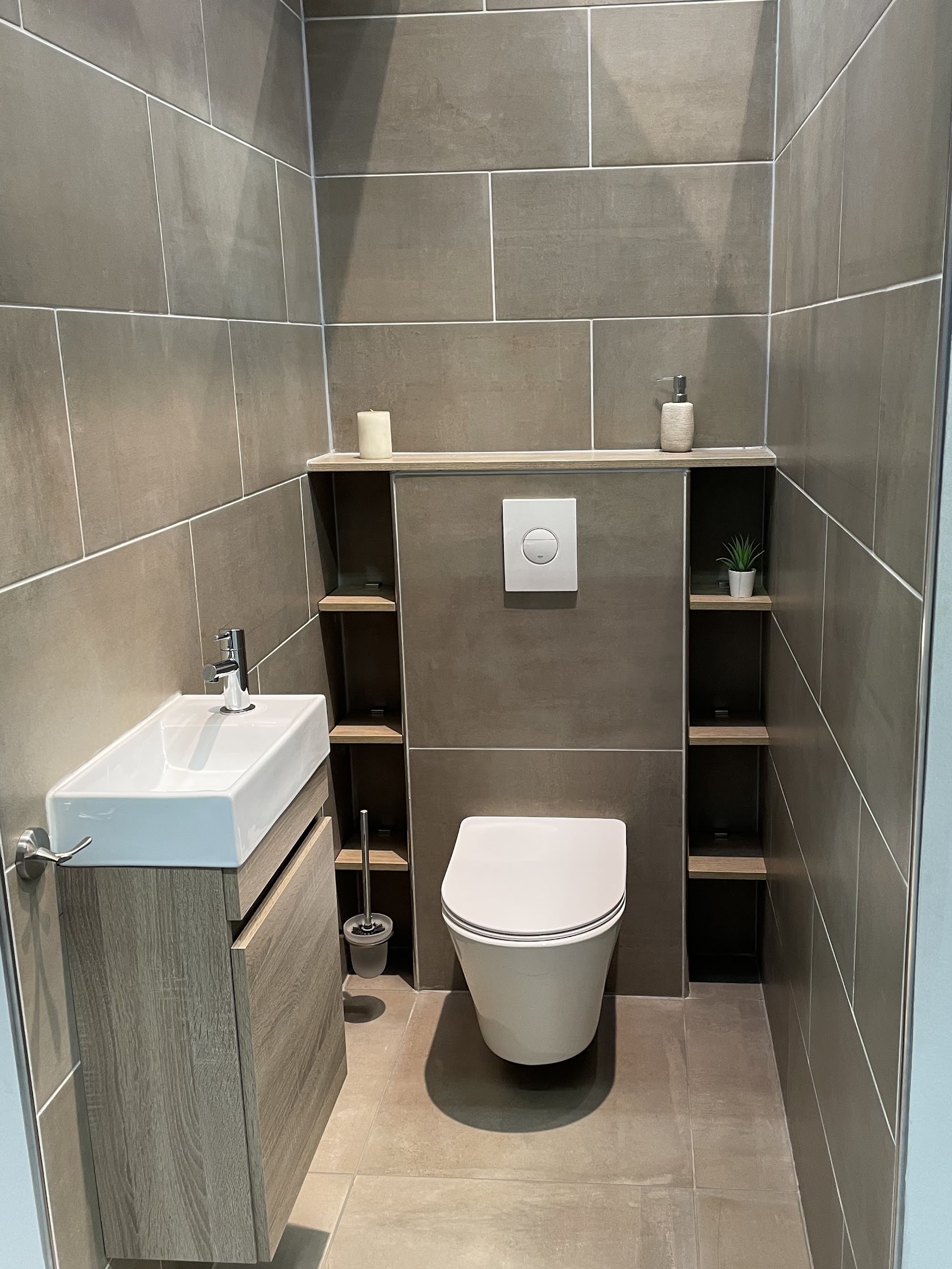 Toiletruimte met grijze wandtegels, zwevend toilet, fonteintje en open vakken