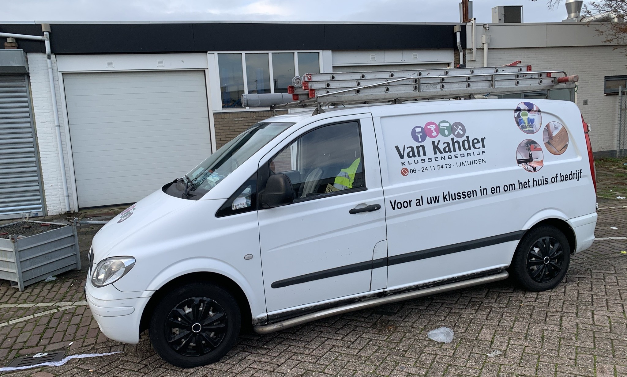 De witte bedrijfsbus van Van Khader klussenbedrijf met ladders op het dak en belettering op de zijkant