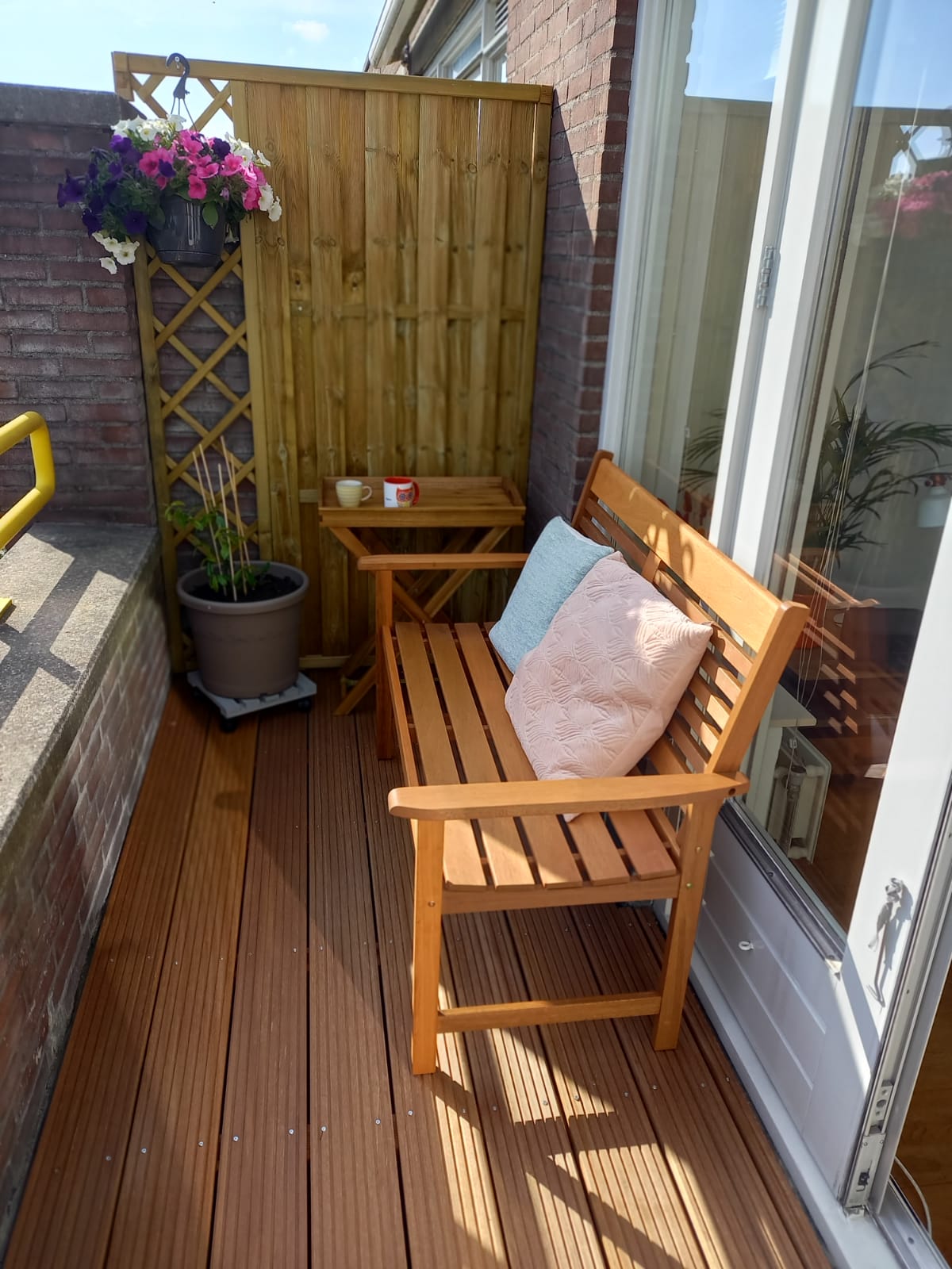 Balkon met houten vlonder, houten scherm, bank en hangende bloemen